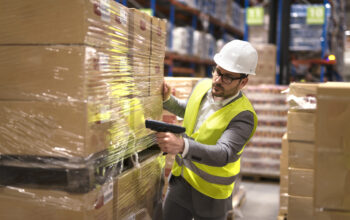 Male warehouse worker using bar code scanner to analyze newly arrived goods for further placement in storage department.