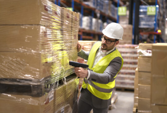 Male warehouse worker using bar code scanner to analyze newly arrived goods for further placement in storage department.